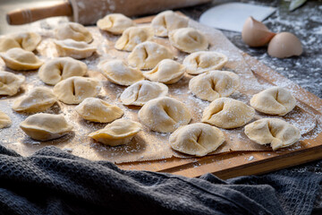 Pelmeni dumplings making process: Raw, uncooked, pelmeni stuffed with meat filling on a wooden, floured board. Gluten free recipe for traditional Russian cuisine. handmade ravioli or dumplings. Side.