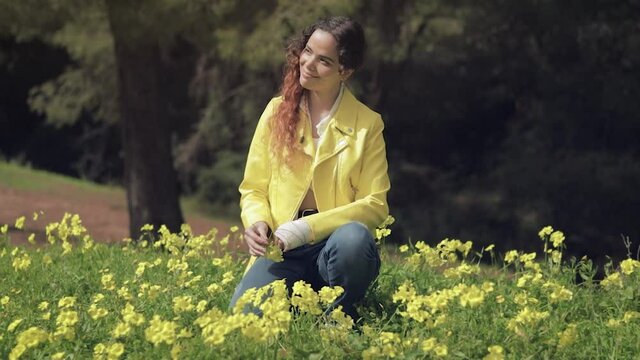 Mujer joven sonriendo y jugando con flores en un prado con flores amarillas en un bosque con &aacute;rboles