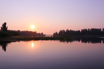 A colorful sunrise over the calm water surface of the lake. Summer landscape. Argazinskoe reservoir, Chelyabinsk, Russia