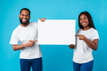 Black couple holding and pointing at blank white advertising placard