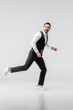 full length view of fashionable muslim man looking away while running on grey