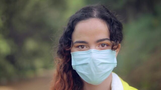 mujer joven gemela se quita la mascarilla y sonr&iacute;e de alegr&iacute;a en un bosque con &aacute;rboles en el fondo