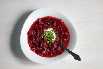 red beetroot soup borscht with scallion, sour cream, spoon in plate on white table