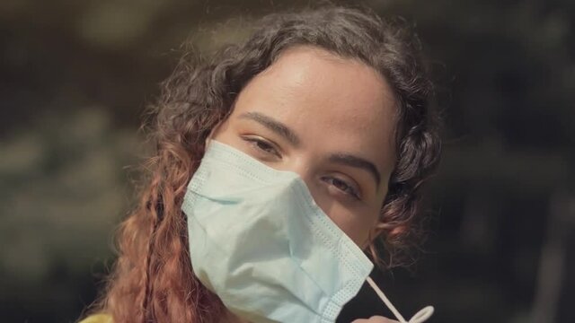 mujer joven gemela se quita la mascarilla y sonr&iacute;e de alegr&iacute;a en un bosque con &aacute;rboles en el fondo