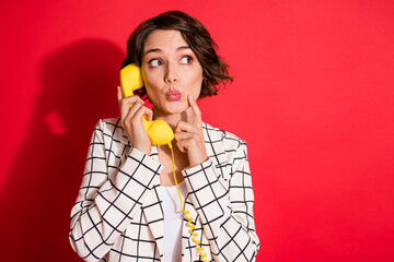 Photo of young attractive woman curious look empty space talk telephone handset isolated over red color background