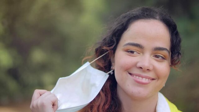 mujer joven gemela se quita la mascarilla y sonr&iacute;e de alegr&iacute;a en un bosque con &aacute;rboles en el fondo