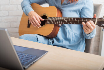A woman teaches to play the guitar online. Remote music lessons on a laptop