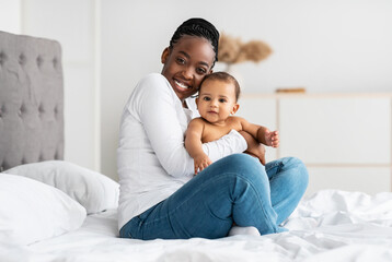 Fototapeta na wymiar Black mom sitting on bed with her cute baby