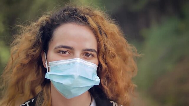 mujer joven gemela se quita la mascarilla y sonr&iacute;e de alegr&iacute;a en un bosque con &aacute;rboles en el fondo