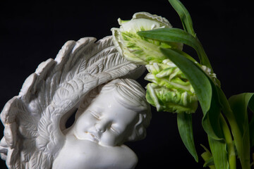 Close up of a white angel with tulip flowers on a dark background. Moment of grief at the end of a life. Last farewell. Funeral concept. Condolence card.