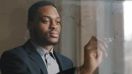 Portrait confident focused serious afro business man student engineer scientist writing math formula on transparent glass wall board using black marker, analyzing project, creating marketing strategy - Powered by Adobe