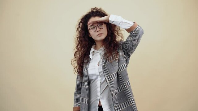 Curious teenager, attentive with her hand over her head, attentive, amazed woman, who discovers us, looking. Cretaceous in gray jacket and white shirt, with glasses posing isolated on a beige