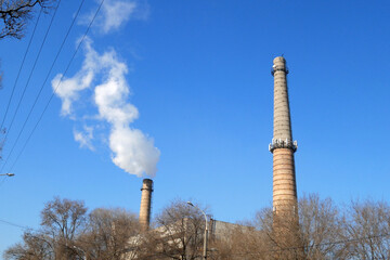 plant tubes with gray smoke on blue sky, chemical plant towers of nuclear power plant against the...