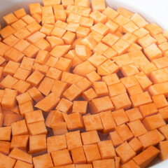 Diced sweet potatoes soaking on a counter in a gray bowl of water waiting to be cooked in a home kitchen.
