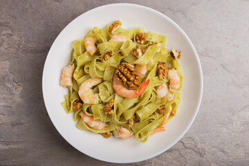 Dish of Fettuccine pasta with shrimp, pesto sauce, walnut on white plate on stone table. Top view. Mediterranean cuisine.