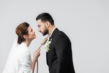 Side view of smiling bride holding slip knot on neck of muslim groom isolated on grey