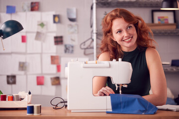Smiling Female Student Or Business Owner Working In Fashion Using Sewing Machine In Studio