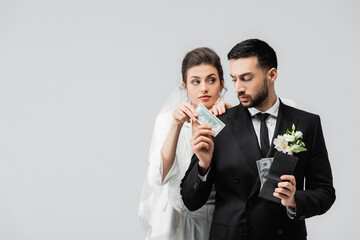 Muslim groom holding wallet and giving dollar banknote to bride isolated on grey