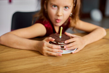 A greedy little girl is wearing a birthday hat hold at a Birthday Cake, make faces