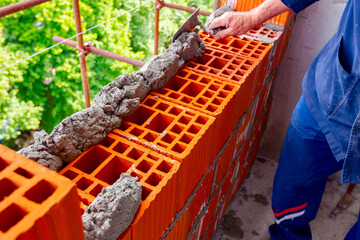 Fototapeta na wymiar Builder using spatula to set up mortar over red brick
