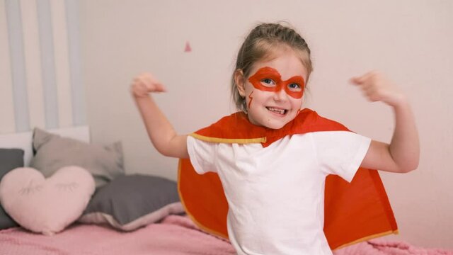 Funny little super hero girl in a red cloak. Superhero concept. Little child playing hero in the home