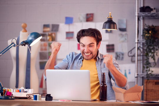 Male Owner Of Fashion Business Celebrating Good News During Video Call On Laptop In Studio