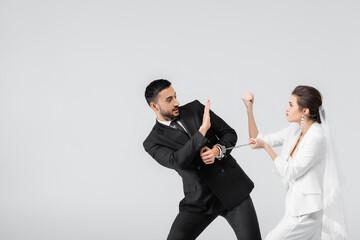 Bride with handcuffs showing fist to muslim groom showing shop gesture isolated on grey