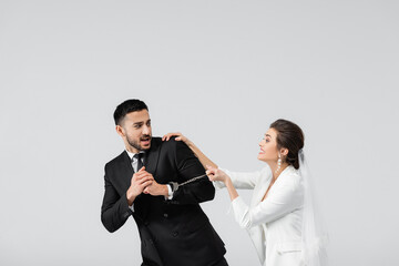 Scared arabian groom in handcuffs looking at cheerful bride isolated on grey