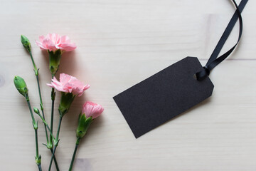 Mockup template with black blank empty clothes label with pink flowers on wooden background.
