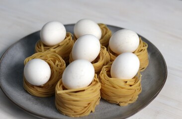 Fresh white eggs in raw spaghetti nests on plate as ingredients for Easter pasta
