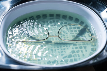 Ultrasound cleaning of glasses in solution. Optical technician repairs the frame of glasses