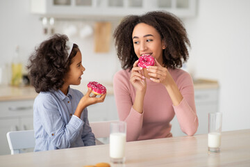 Black mother and daughter eating sweets in kitchen