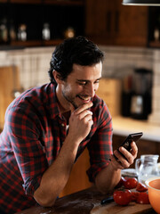 Young man preparing breakfast and using the phone. Man reading news online in the morning..