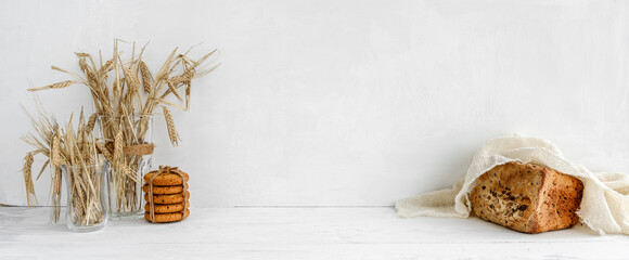 White kitchen banner - oatmeal cookies, grain bread and ears of grain on a white table.