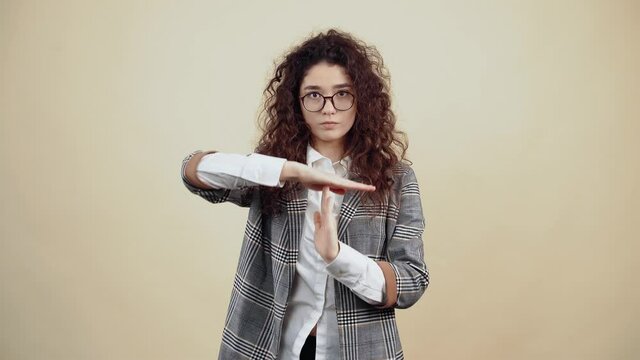 The young businesswoman with her hands points to the stop. Cretaceous in gray jacket and white shirt, with glasses posing isolated on a beige background in the studio. The concept of people's