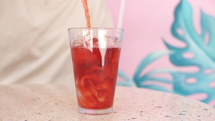 Pouring strawberry ice tea to a glass with ice cubes 