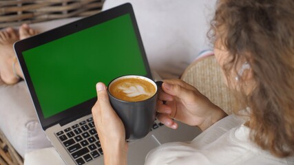 Top view of female sitting with mug of cappuccino working on her laptop. Remote work concept. Green screen 