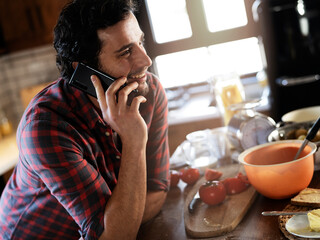 Young man talking to the phone in the kitchen. Man preparing breakfast at home..