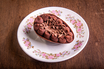 Mini stuffed chocolate easter egg with grated chocolate on the top on a white plate with flowers design on a wooden table.