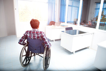 A side view of a Thai-Asian man working from work using a wheelchair, simple gray interior with copy space.