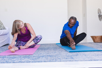 Diverse senior couple exercising sitting on yoga mats stretching
