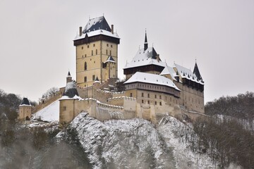 Karlstejn Castle shown in winter, dusted in snow with cold white skies behind, Beroun DIstrict, Central Bohemia, Czech Republic. - obrazy, fototapety, plakaty
