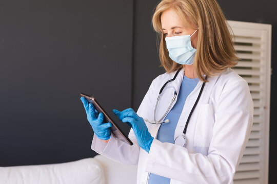 Caucasian senior female doctor wearing face mask using digital tablet