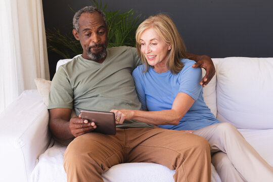 Diverse senior couple sitting on couch and using digital tablet