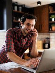 Happy man drinking coffee and using the laptop. Handsome man talking to the phone..