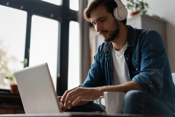 Man Using Laptop Wearing Headphones Relaxing Sitting On Sofa At Home.