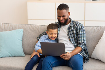 African Daddy And Son Watching Cartoons On Laptop At Home