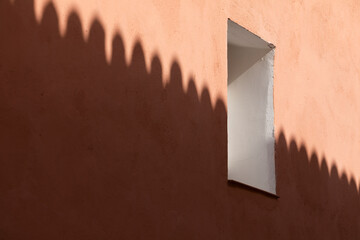 Photograph of a window opening, and the silhouette shadow of the adjoining roof, on the pink and salmon painted facade, in a house in Ambel, a small town in the Campo de Borja region, Spain.