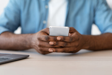 Closeup Shot Of African American Man Sitting At Desk And Using Smartphone