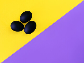 Black eggs on the yellow and violet background. Easter, diversity, geometric, pattern, food concept